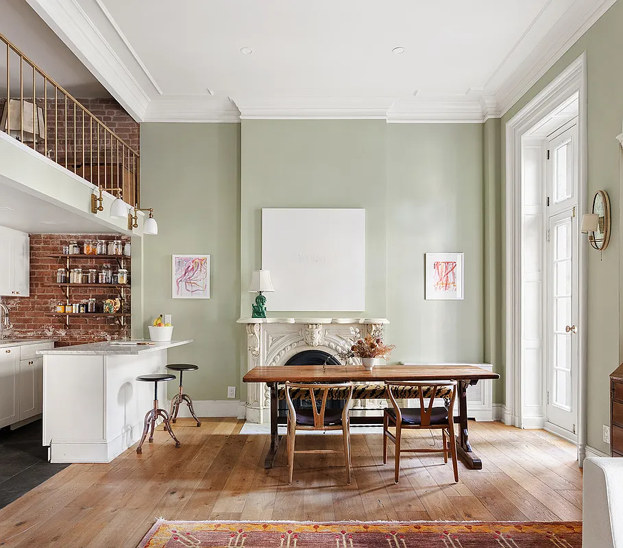 the living area with a marble mantel next to the open plan kitchen with a glimpse of the loft above