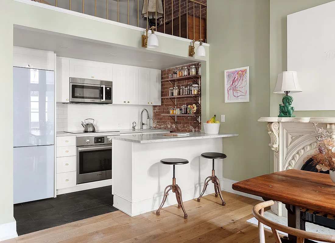 compact kitchen with white cabinets, peninsula with bar seating and a wall of exposed brick