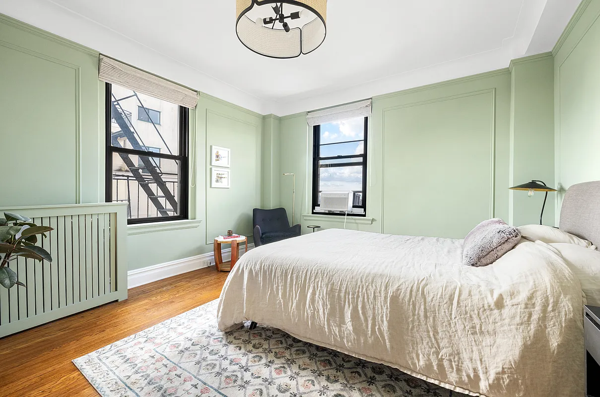 bedroom with pale green walls, wall moldings, wood floor