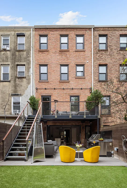 brick rear facade and a view of the paved patio with seating and an outdoor kitchen